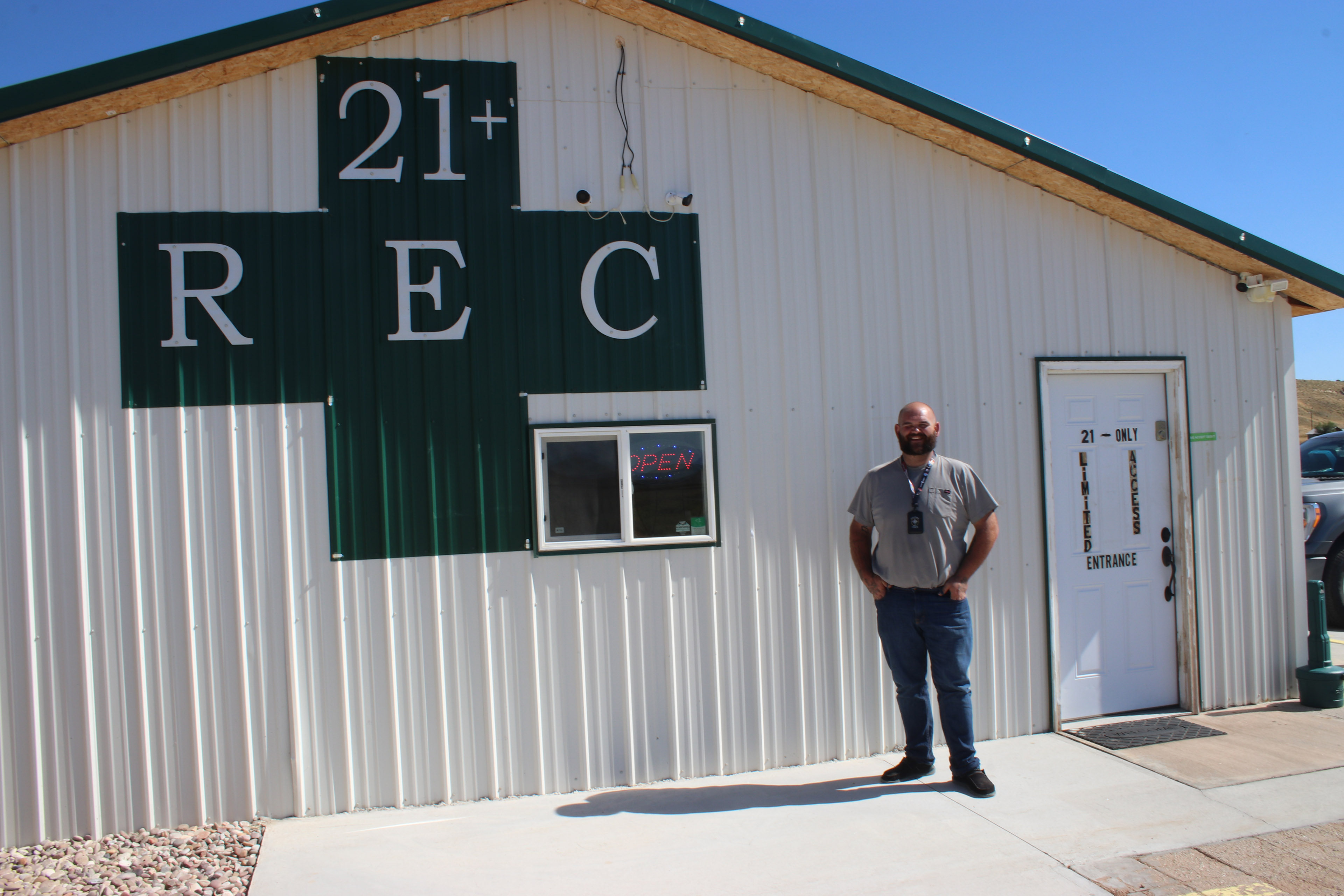 Lando Blakley stands outside his retail marijuana store, Dino Dispensary. On the side of the store is a large green medical cross, which inside reads: "21+ REC"