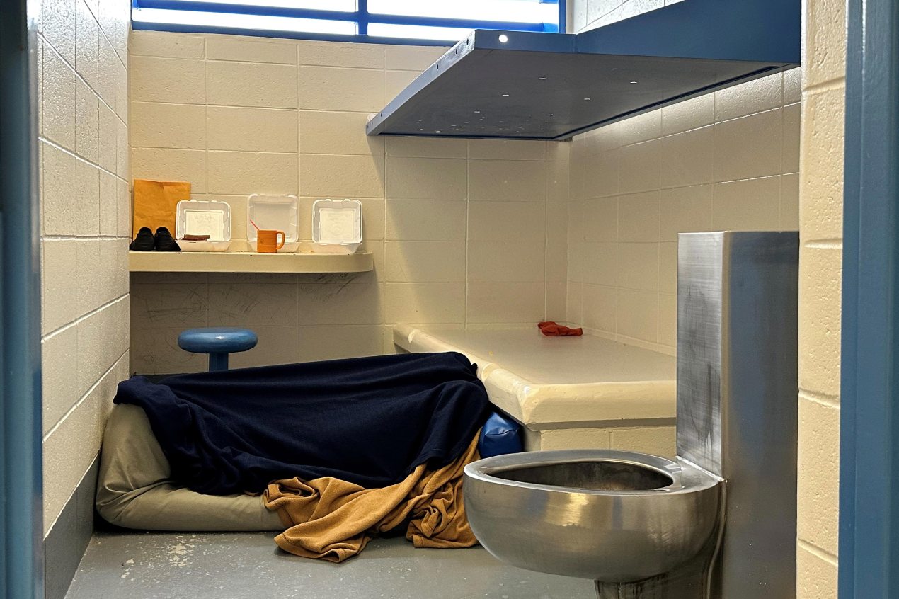 A photo of someone lying under a blanket in a jail cell.