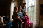 A photo of a mother, father, and two children standing by a window.