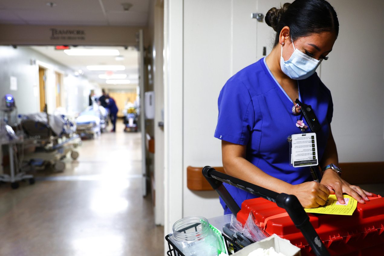 A photo of a lab technician writing a note while wearing a surgical mask and scrubs inside a hospital.