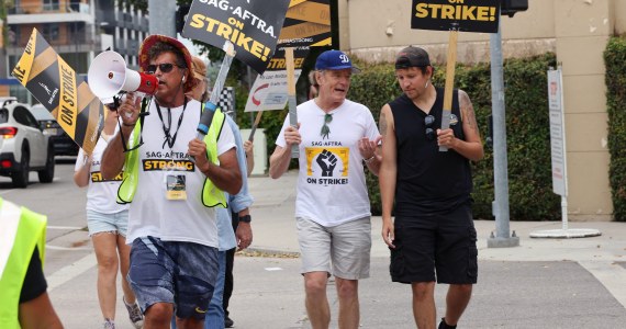 A photo of people walking outside and holding signs that say, "SAG-AFTRA on strike!"