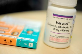 A photograph shows a white pill bottle of Harvoni, a drug to treat hepititis C.