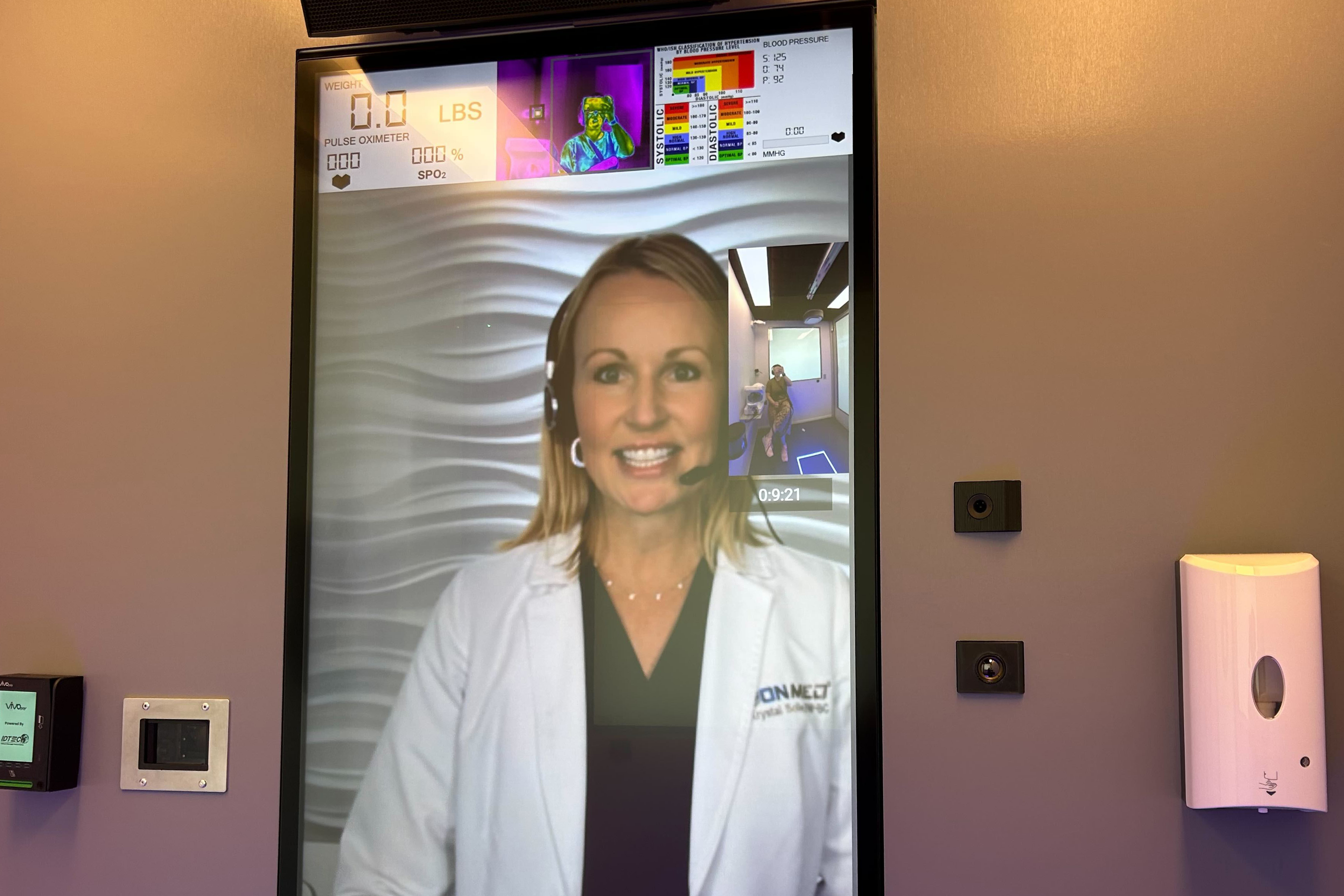 A photo of a medical worker appearing on a large screen via video call.