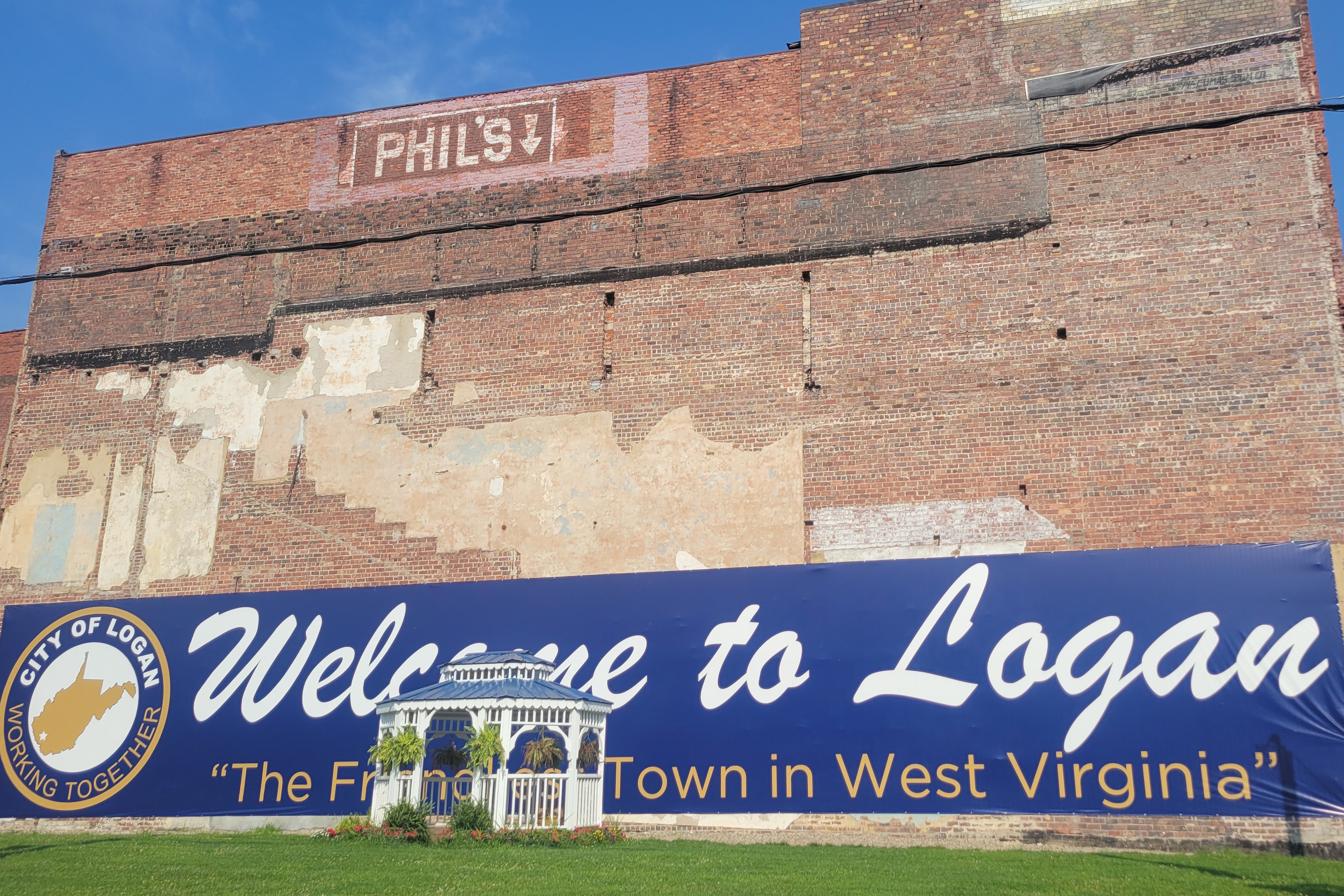 A photo of a brick wall with a poster that reads, "Welcome to Logan." A gazebo rests in front of it.