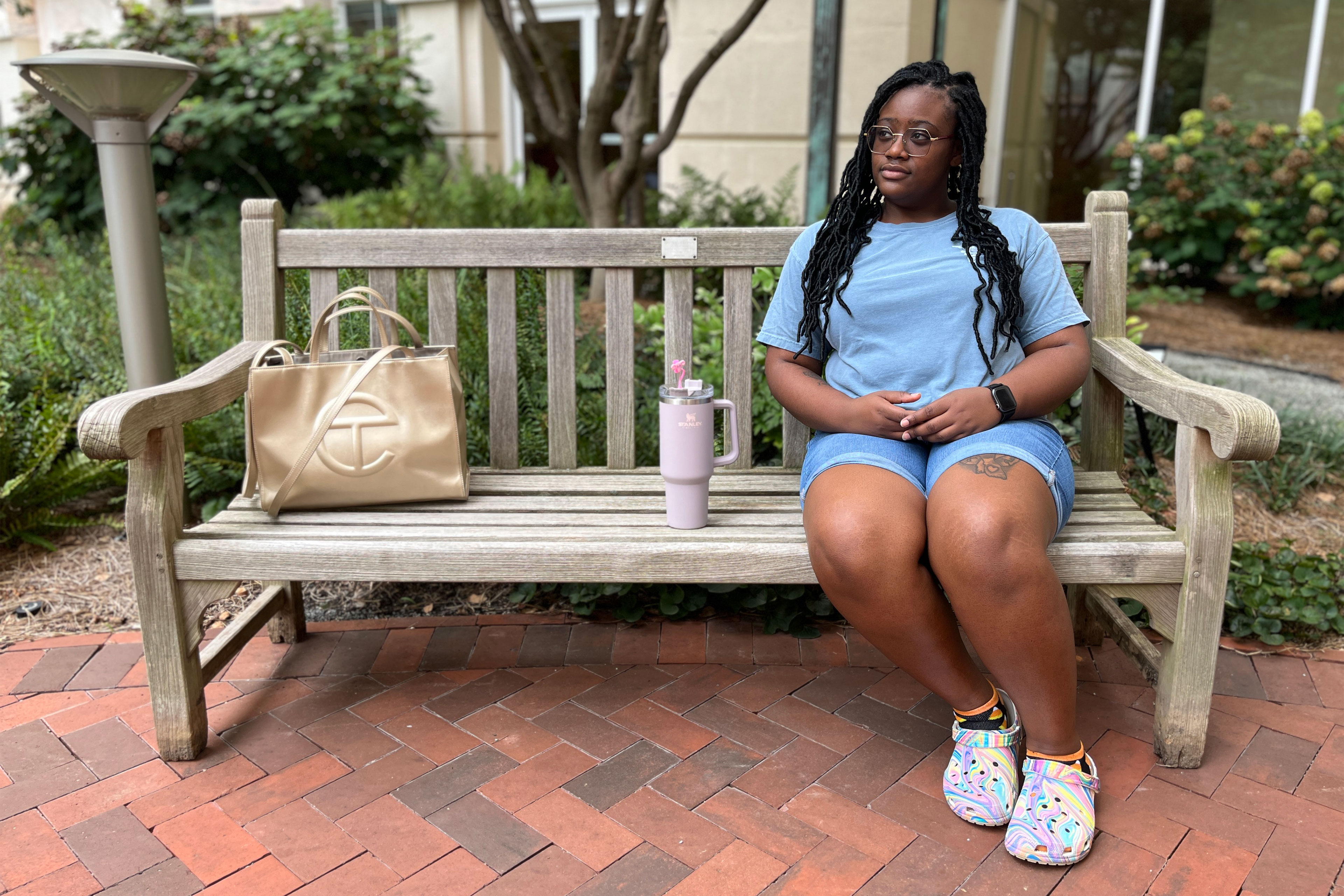 Alexis Perkins sits outside on a park bench in a courtyard.