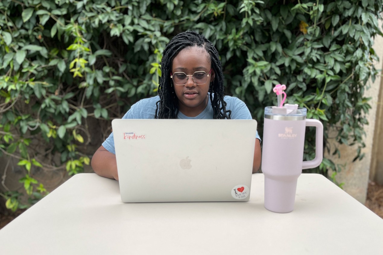 Alexis Perkins is sitting at a table outside and is using her computer.
