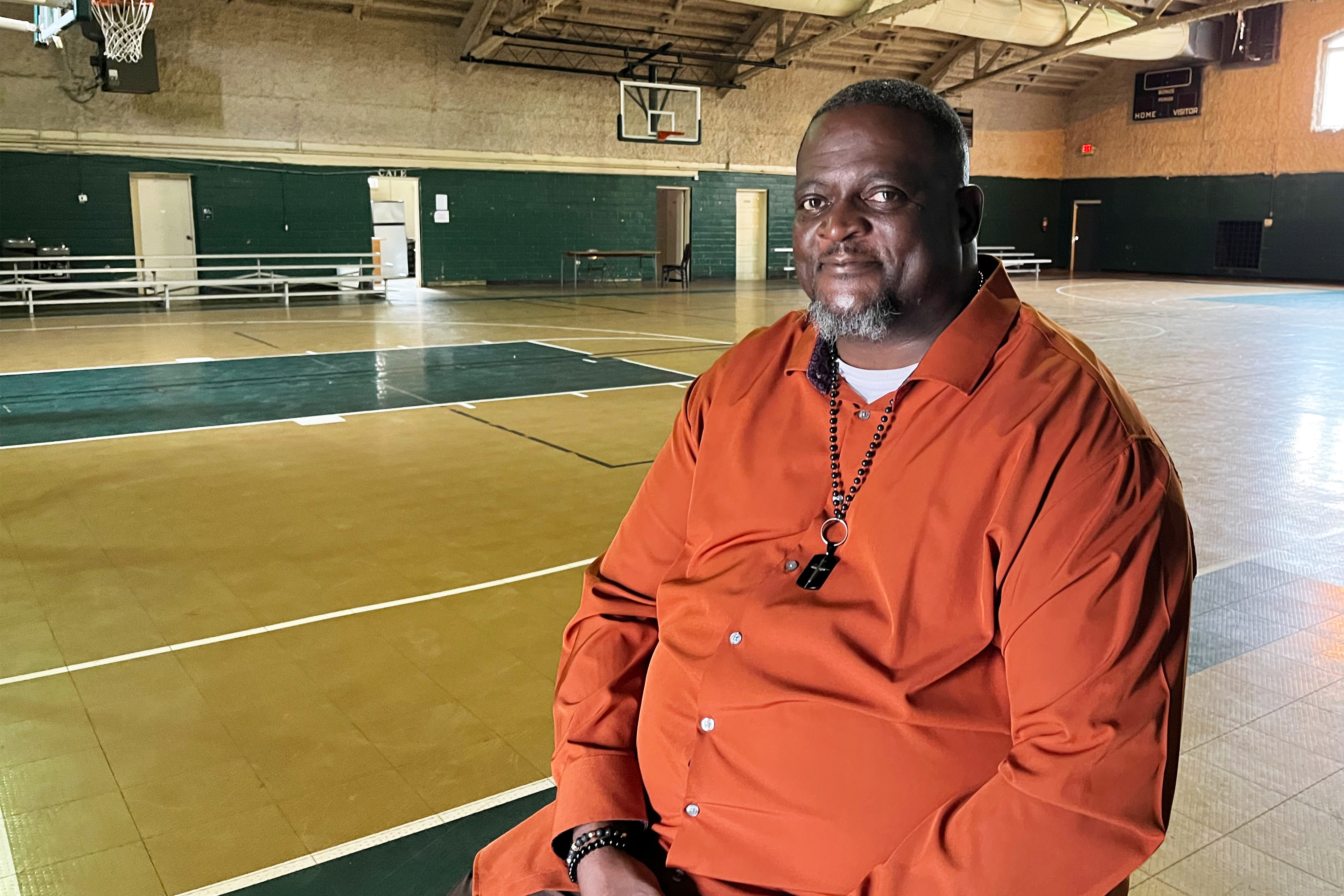 A photo of a man sitting for a photo indoors at a basketball court.