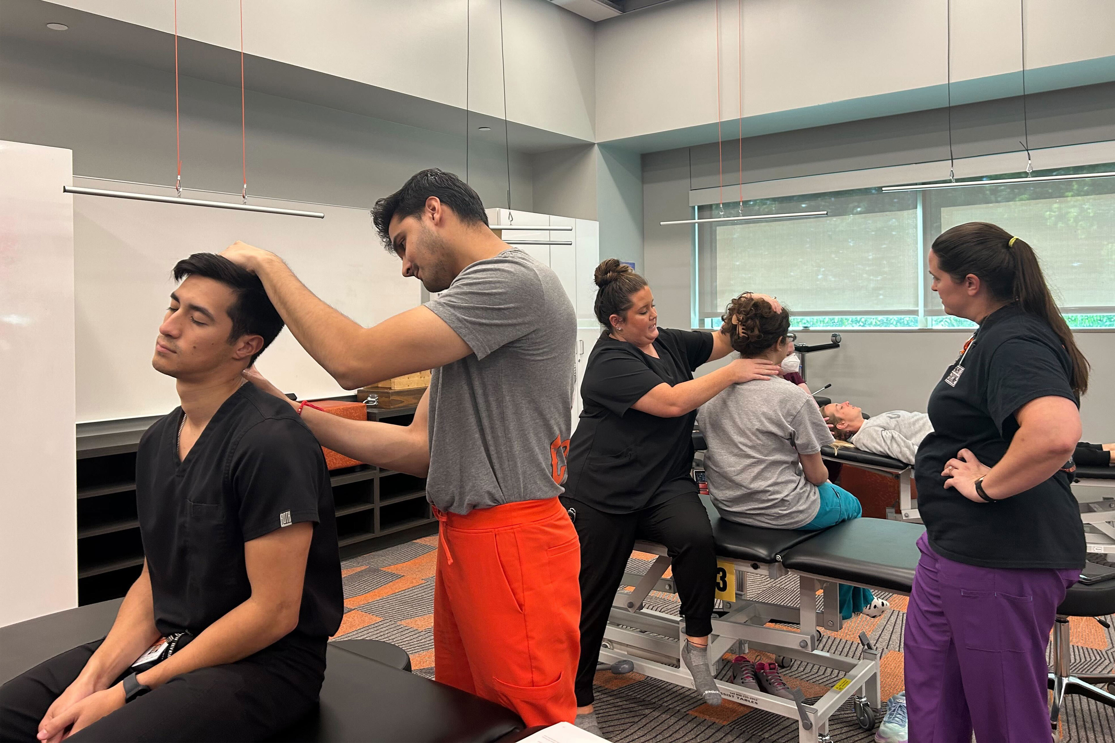 A photo of medical students practicing manipulations while an instructor looks on.