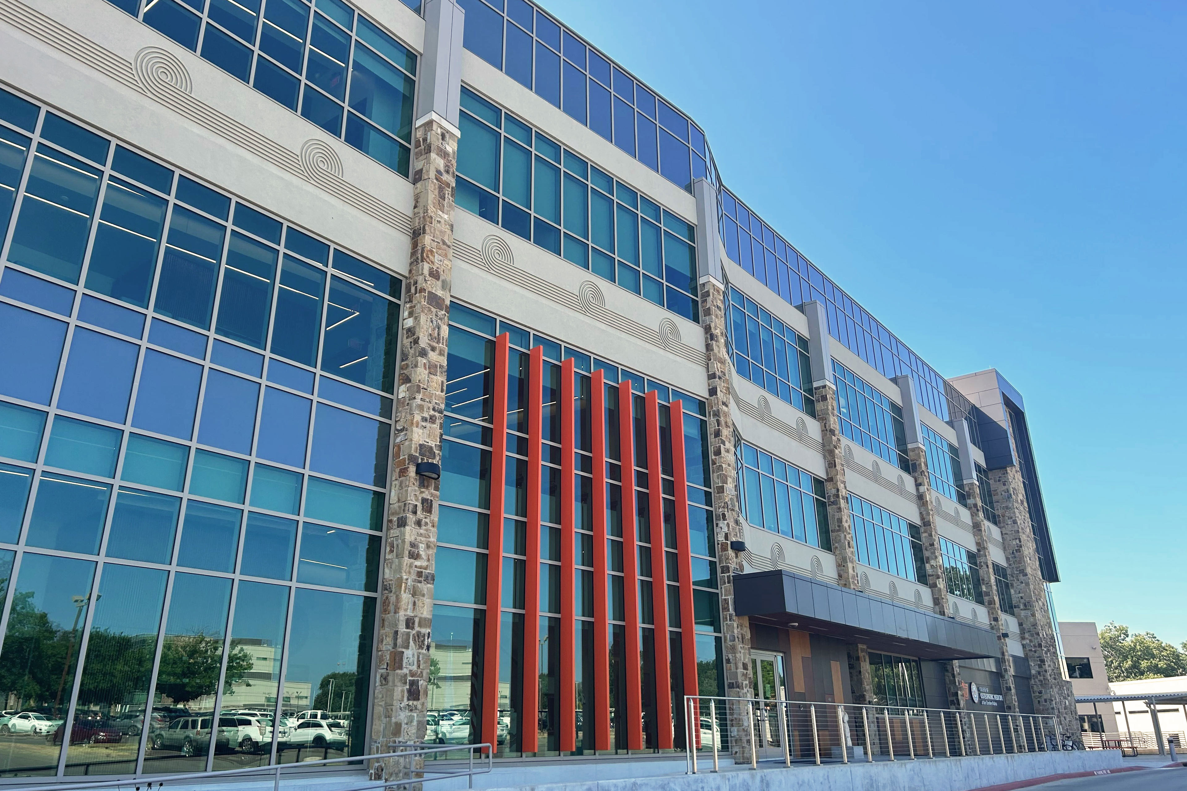 A photo of the exterior of a medical school building. The building has small orange accents and circular symbols carved into sections.