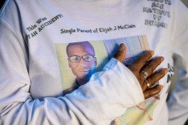 A closeup image of a woman's torso wearing a sweatshirt printed with the photo of a young man and lines of text, including one that reads "Single Parent of Elijah J Mclain".