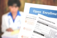 A photo of a patient holding open enrollment forms with a doctor blurred in the background.