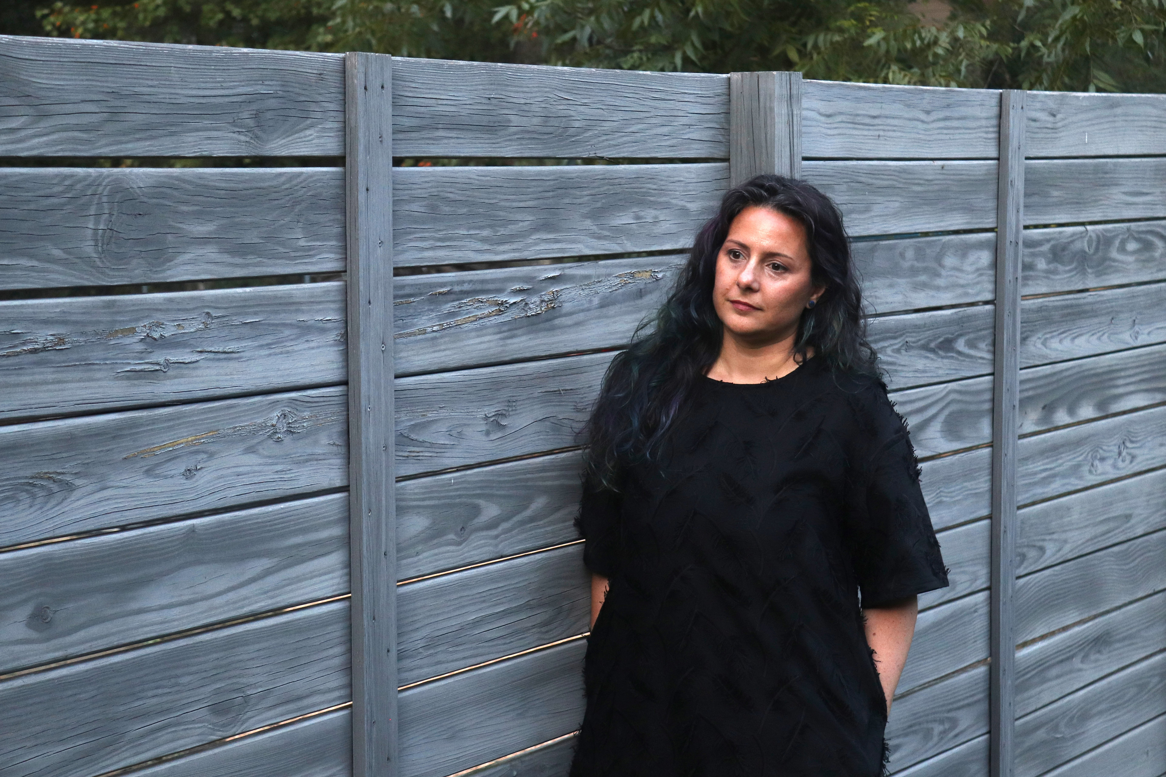 A photo of a woman standing for a photo by a fence outdoors.