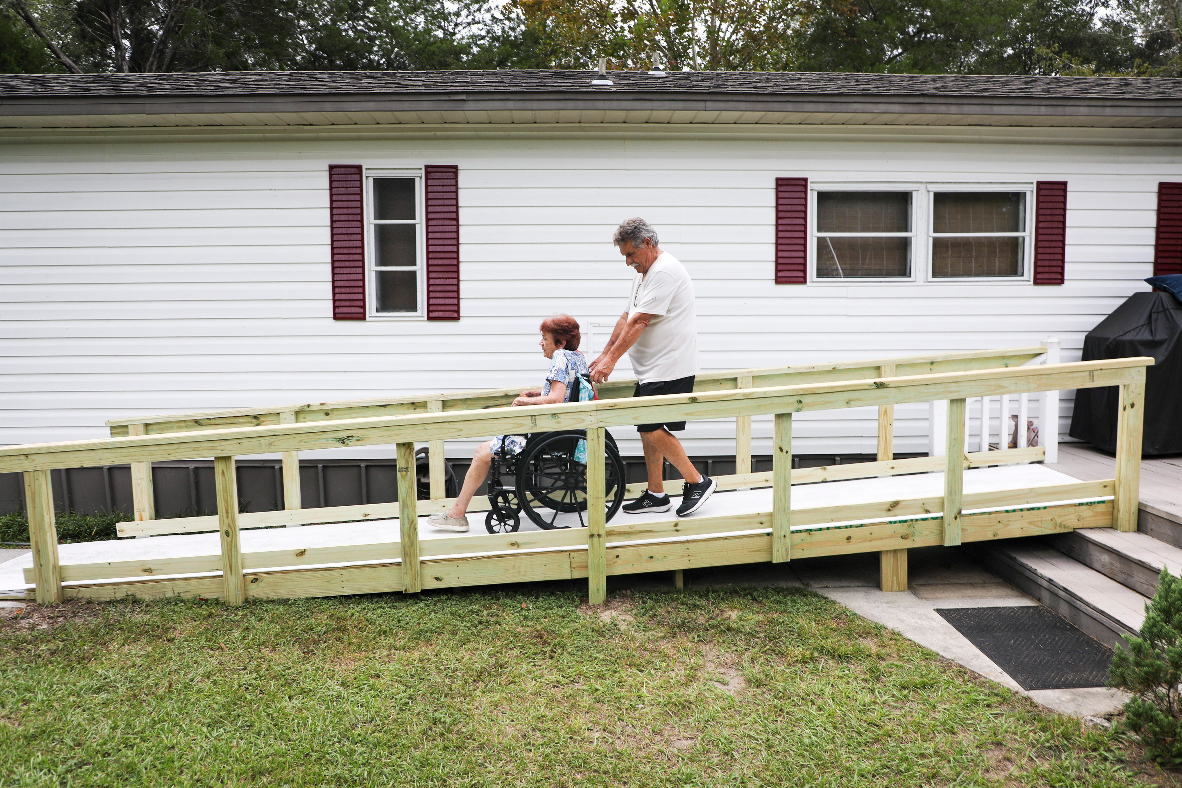 A photo of a man helping a woman in a wheelchair down a ramp.