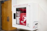 An image of a cabinet on a wall with a glass door and a box reading Narcan and a defibrillator inside.