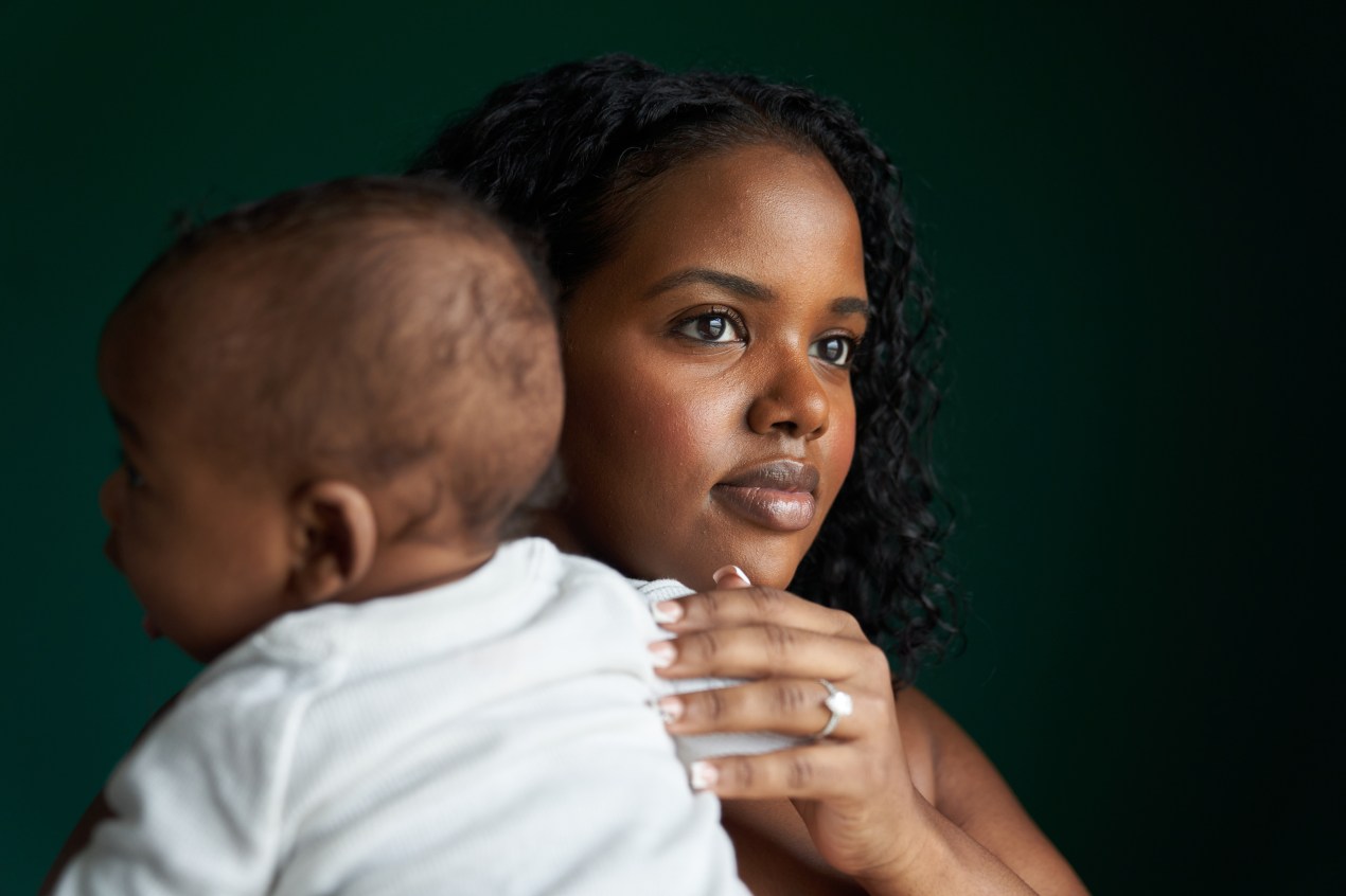 A woman looks into the distance to the right of the frame, while holding her baby on her shoulder