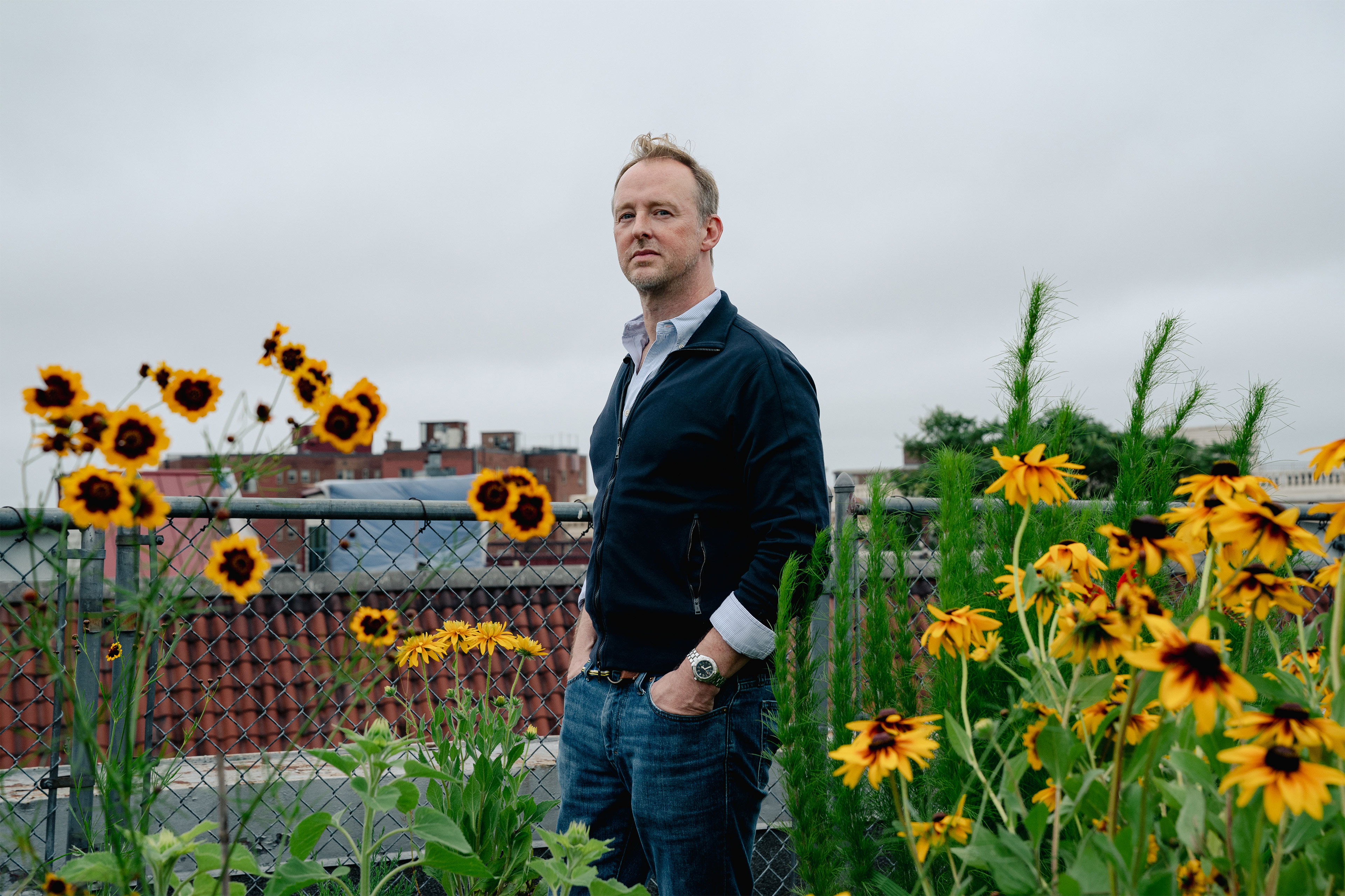 A photo of a man posing for a photo surrounded by black-eyed Susan flowers.