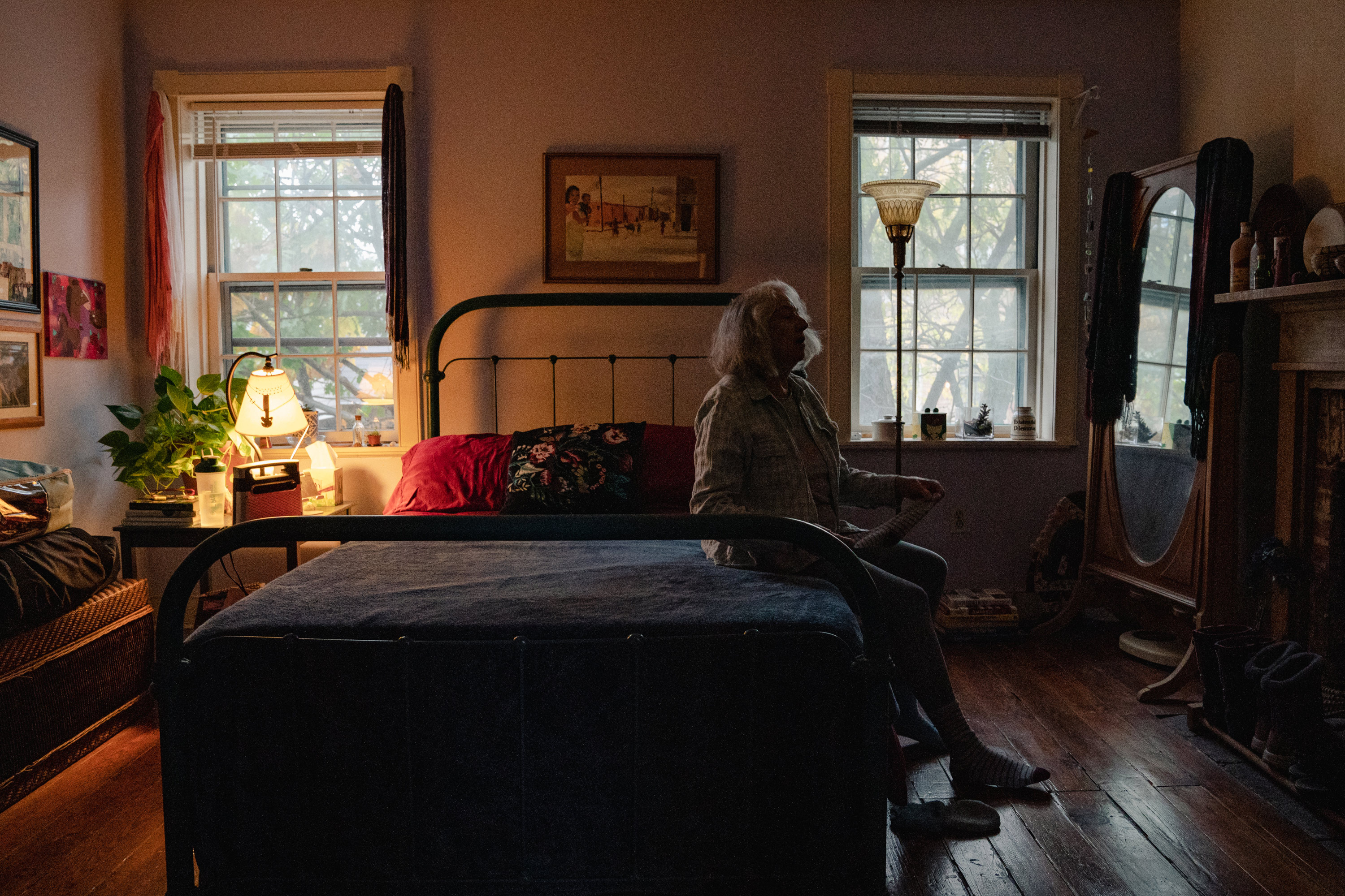 A photo of a woman seated at the end of her bed.