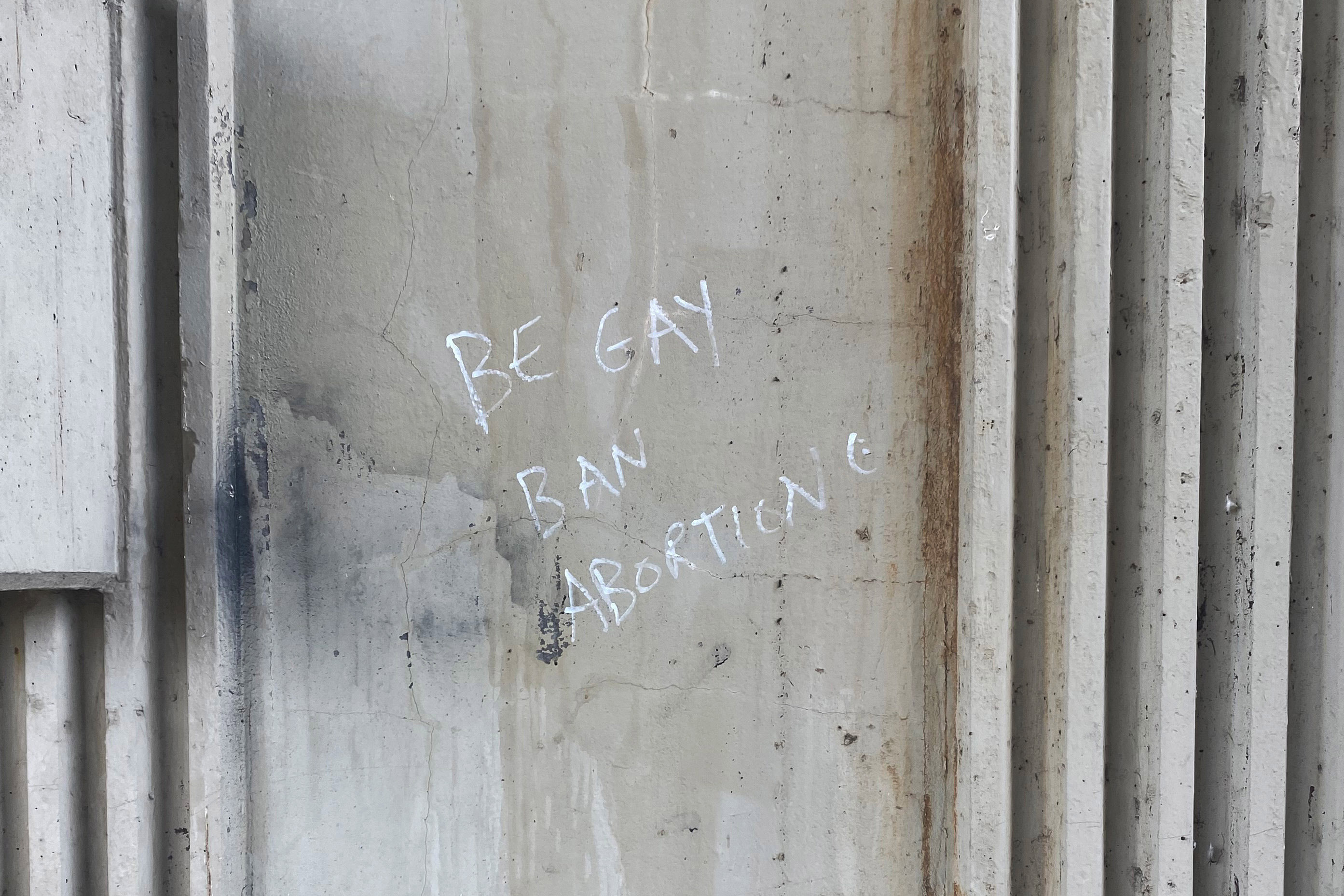 A photograph of graffiti written in white marker on a dilapidated wall. It reads, "be gay / ban abortion."
