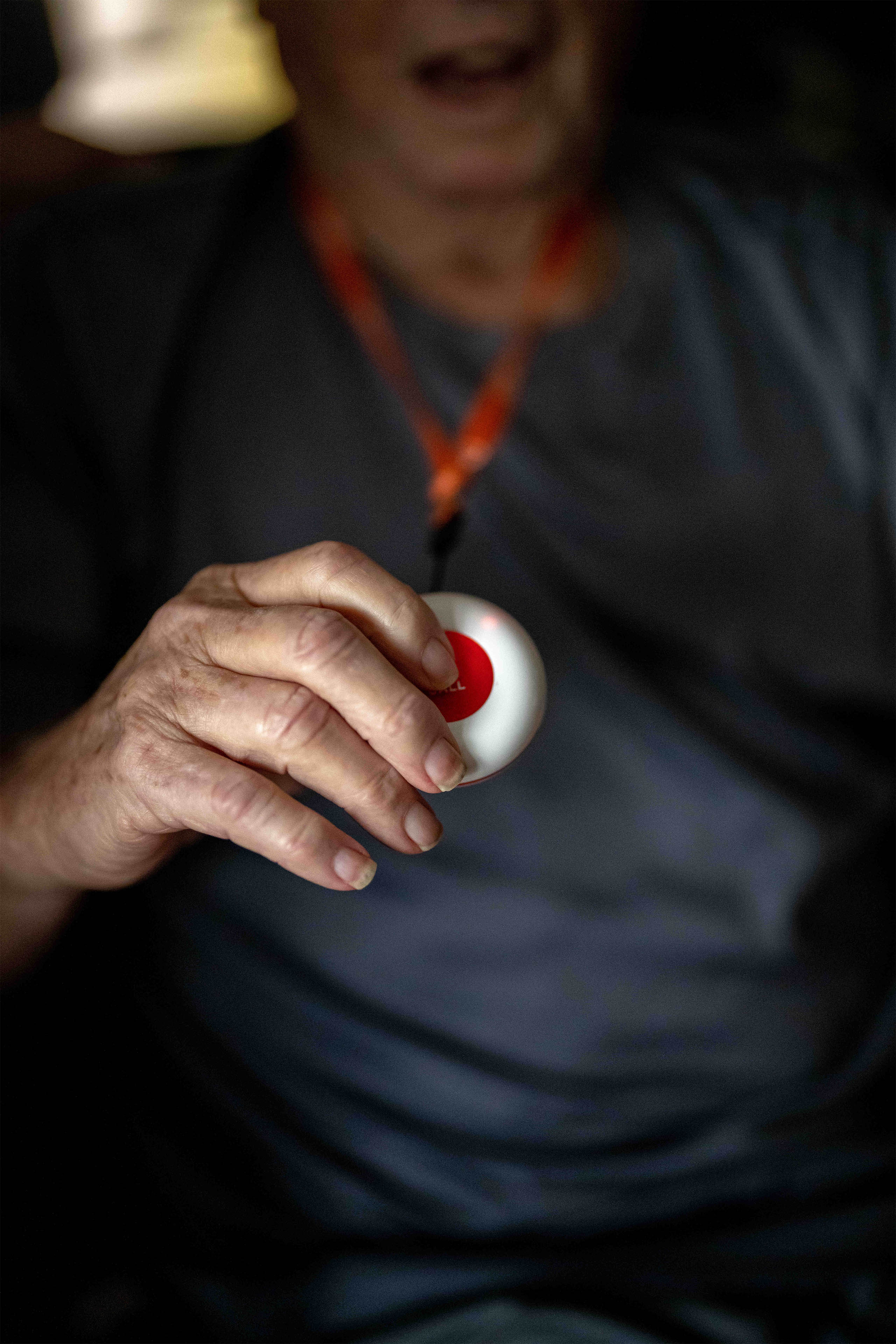 A photo of an elderly man holding up a lanyard with an emergency button on it.