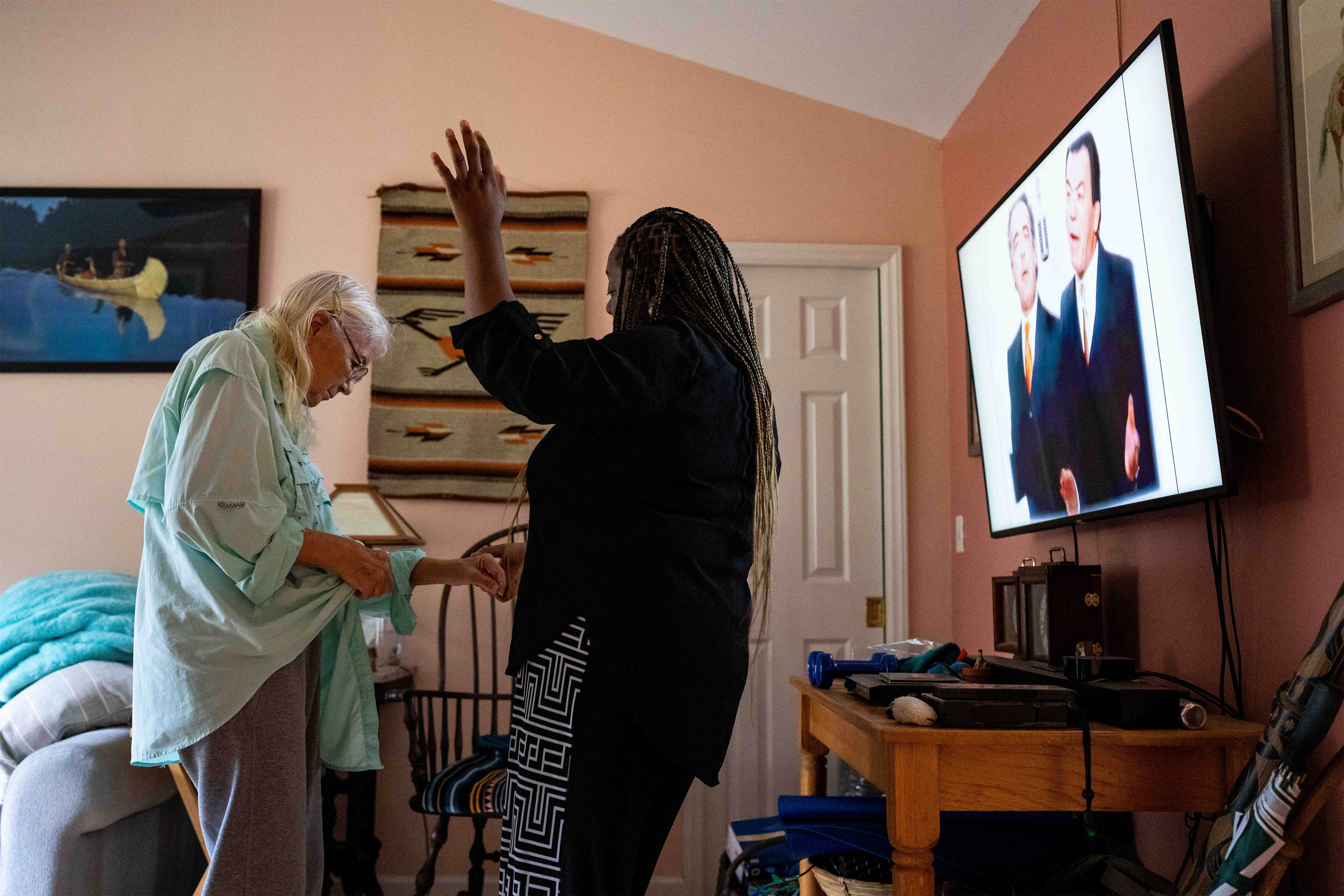 A photo of a caretaker dancing with an elderly woman indoors.