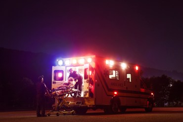 Paramedics lift a person on a stretcher into ambulance at night.