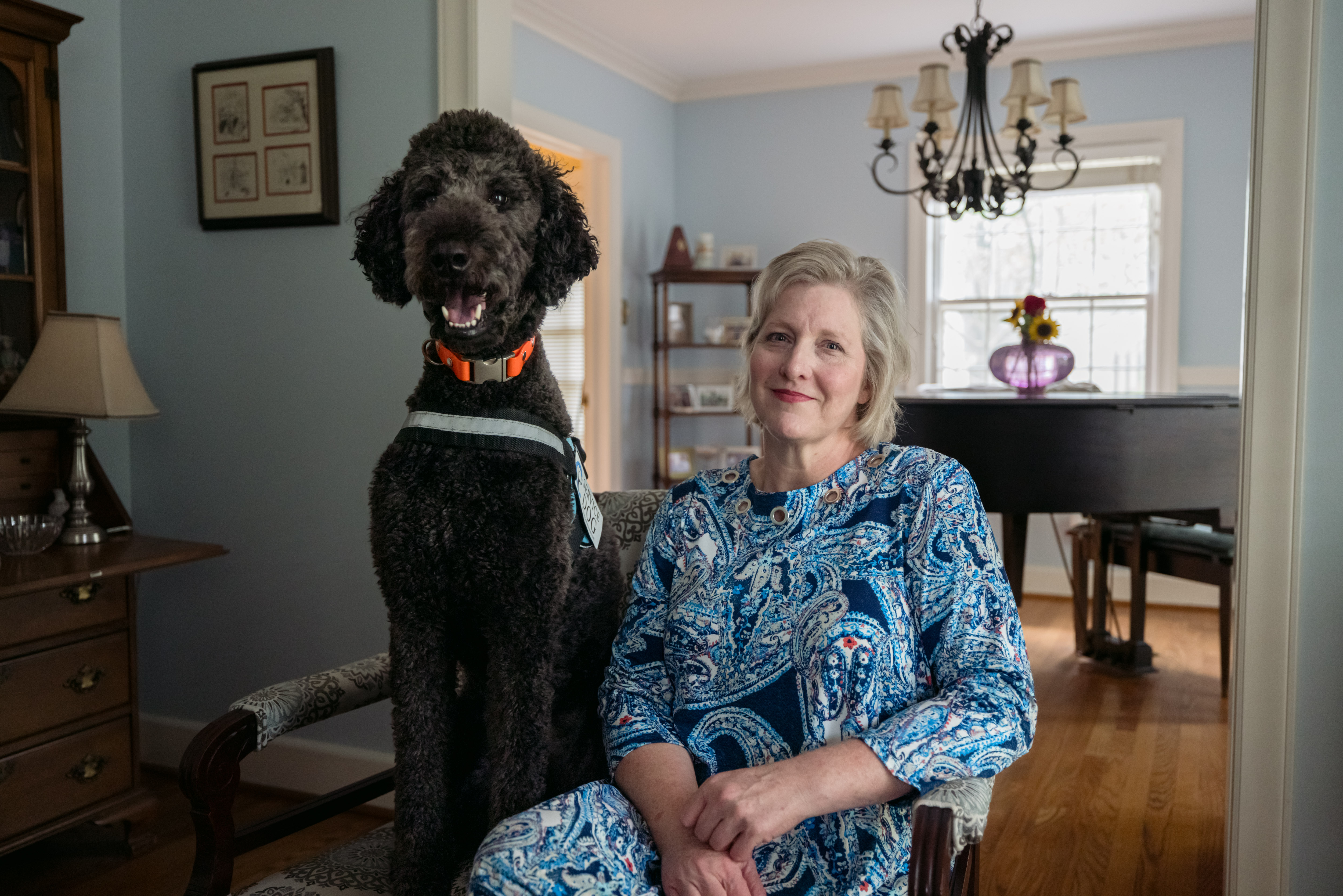A photograph of Sally Nix sitting beside her service dog in her home.