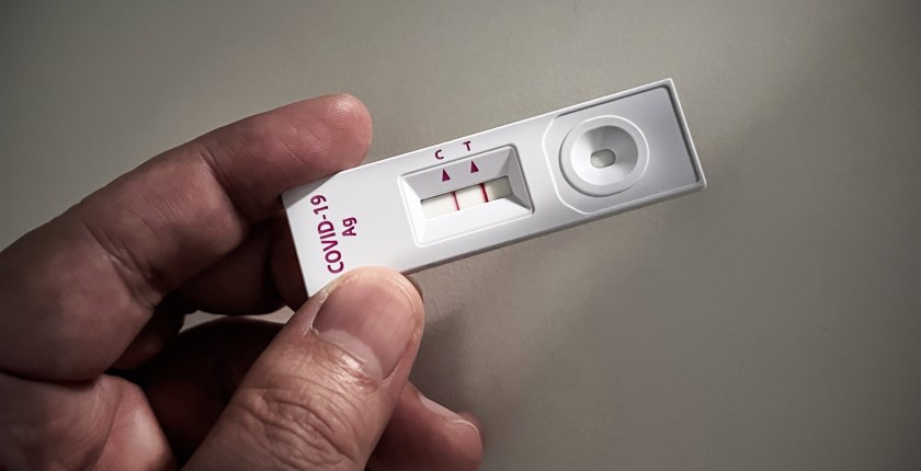 A photo of a person holding an at-home rapid test for covid-19 with a positive result.