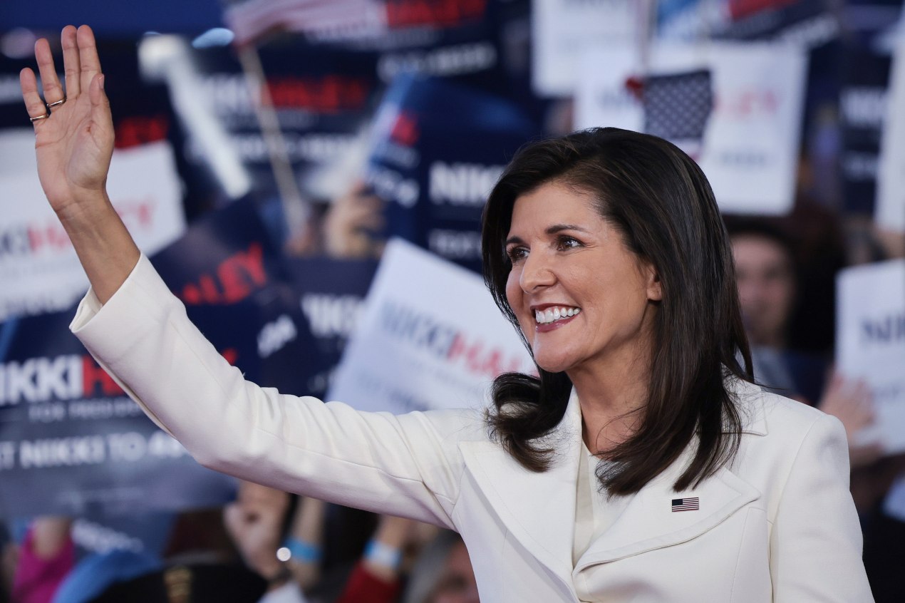 A photo of Nikki Haley waving with supporters behind her holding up signs with her campaign logo.