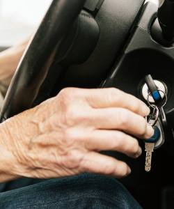 A photo of an older person's hand putting their car key in the ignition.