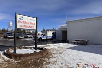 A photograph of the exterior of Lincoln Health. A sign reads, "Emergency Entrance." There are parked ambulances and other cards in the parking lot behind the sign. The ground is covered in melting snow.
