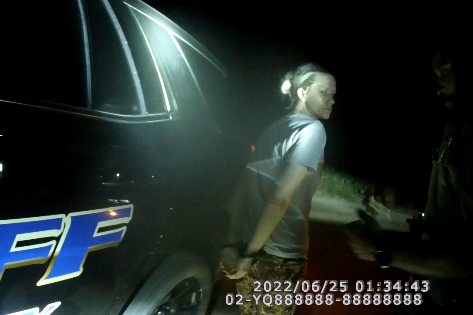 A screengrab of Angela Collier in handcuffs next to a police car at night.