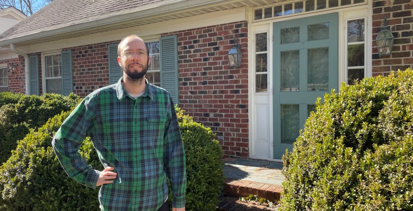 Patrick Dunnagan stands outside his North Carolina home on a sunny day. He wears a plaid shirt and glasses.