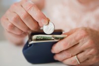 An up close photograph of the hands of a senior woman putting money into a coin purse.