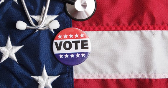 A stethoscope and voting pin rests on top of an American flag.