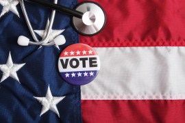 A stethoscope and voting pin rests on top of an American flag.