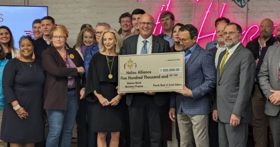 Stephen Loyd, center, stands in a crowd holding a foam-board check for $500,000.00 for the Helios Alliance.