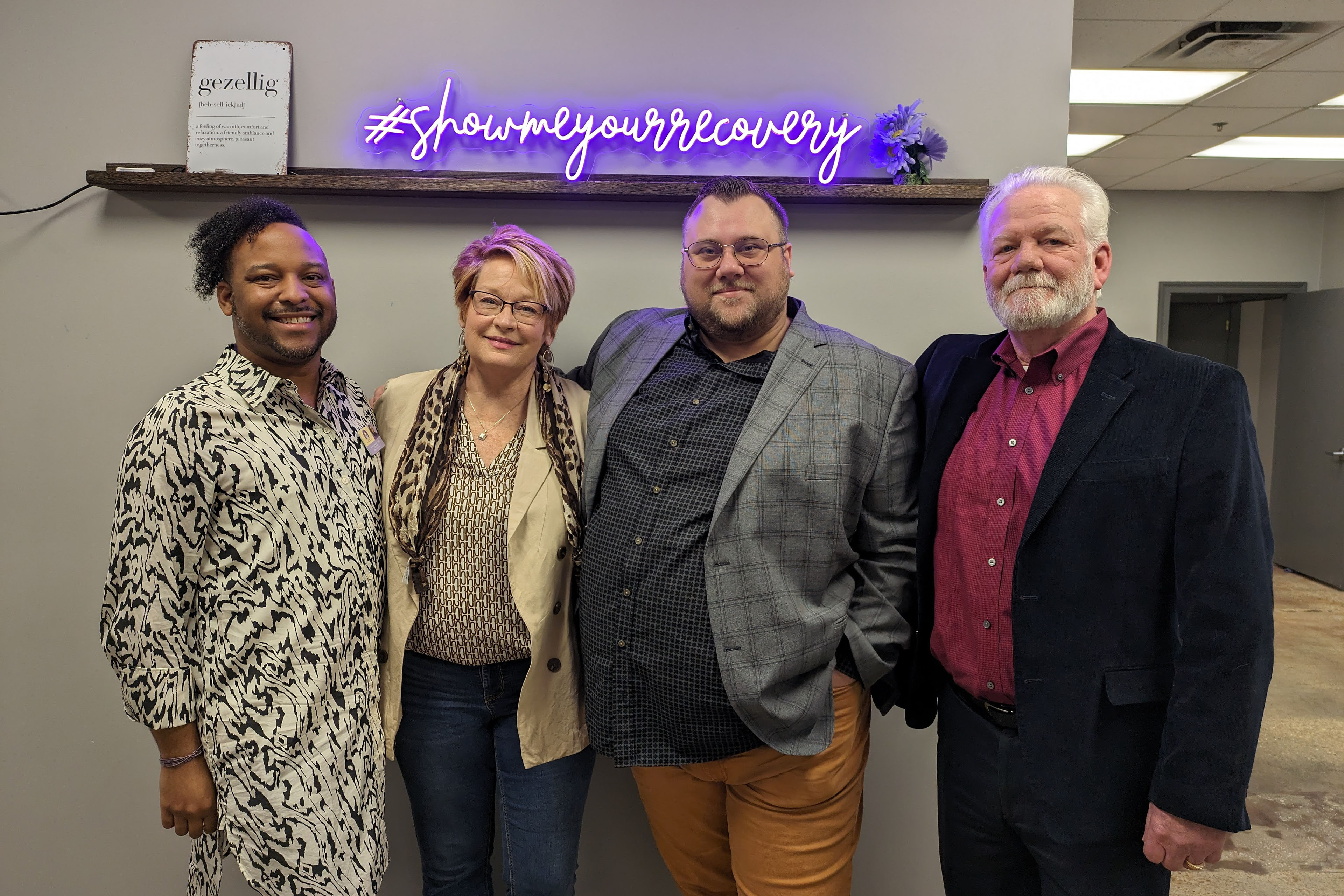 (From left): Devin Burton, Lisa Teggart, Chance Shaw, and Larry Vahle stand side by side in an office room. Above them in a purple neon sign which reads, 