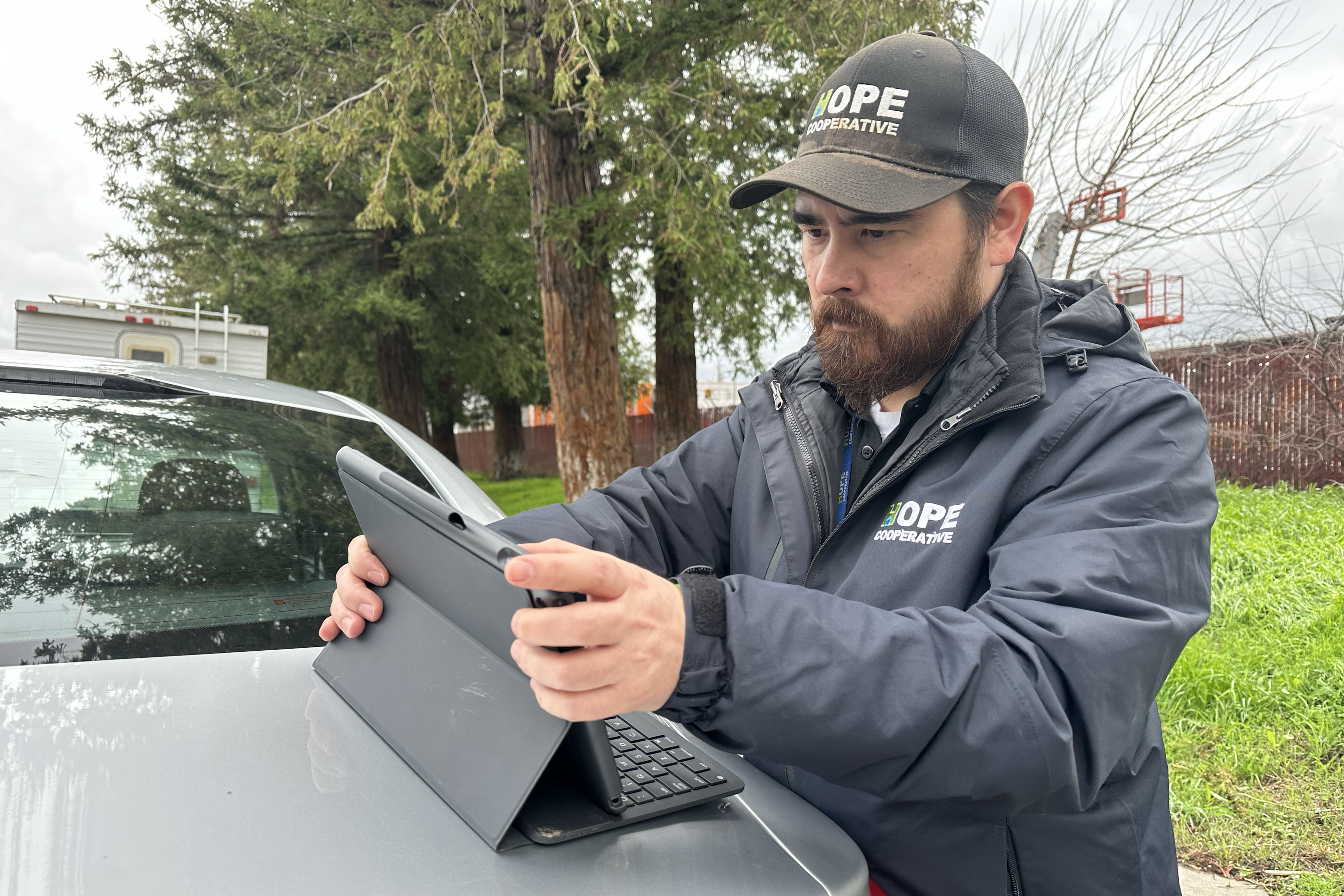 Greg Stupplebeen works on a tablet that is propped up on the back of a car.