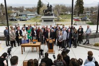 Gov. Greg Gianforte, surrounded by Republican lawmakers, speaks at a bill signing ceremony on the steps of the State Capitol, in Helena, MT. Press huddles in front of the podium he speaks from with microphones and cameras.
