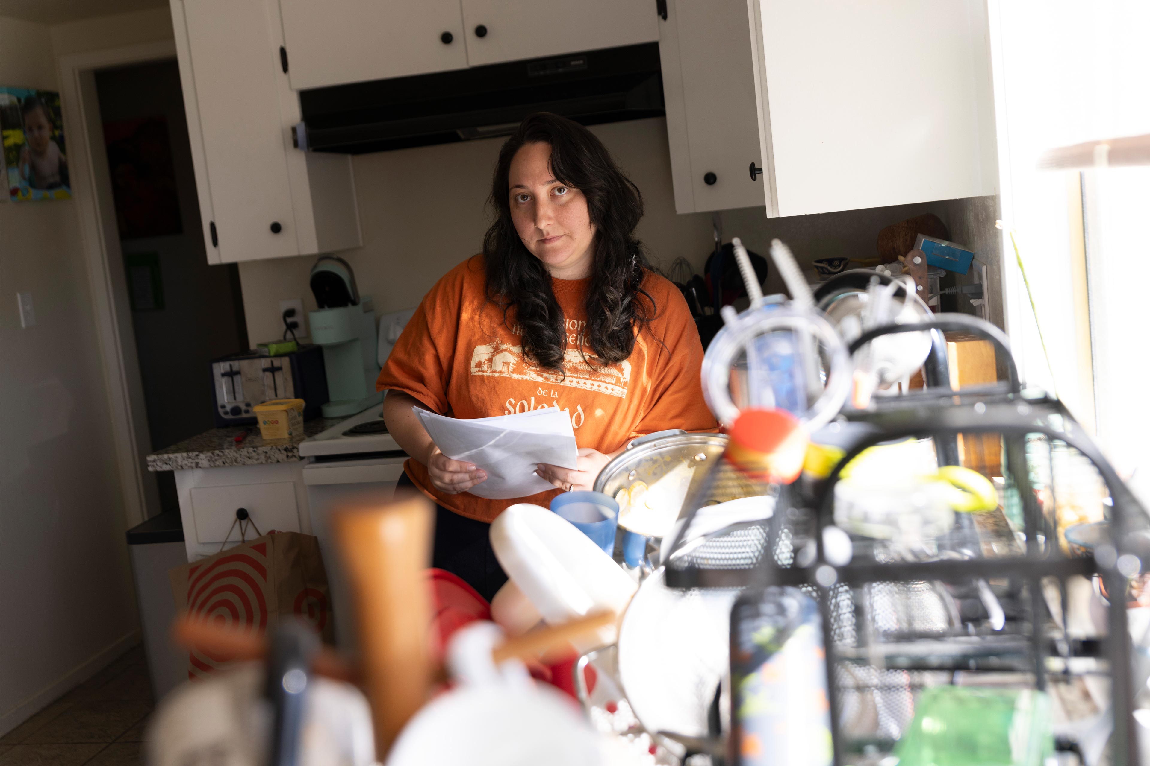A photo of a mother standing in her kitchen holding medical bills