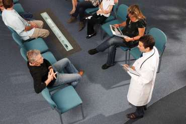 A photo of a doctor speaking to patients in a hospital waiting room.