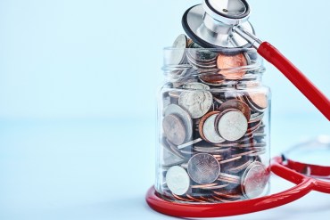 A jar filled with coins is wrapped with a red stethoscope.
