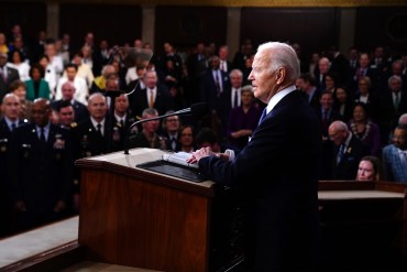 A photo of President Biden speaking at a podium to a crowd seated before him.