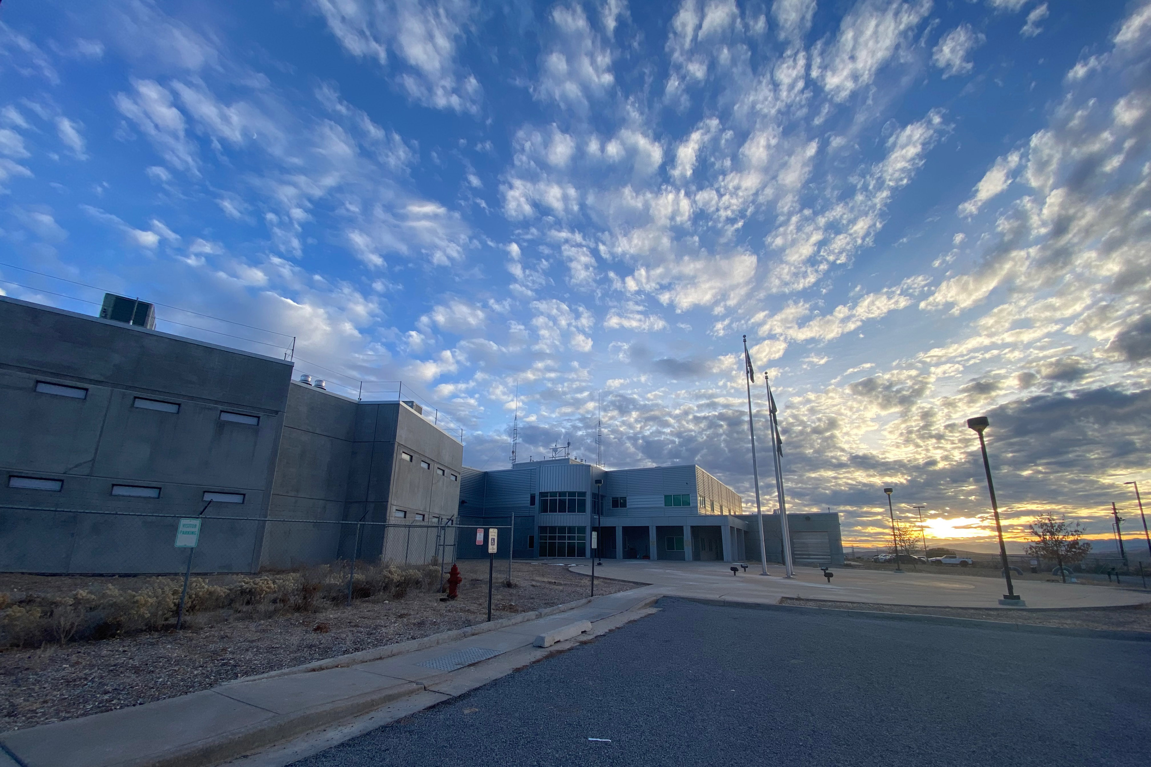 The sun rises over the Sanpete County Jail and Sheriff’s Office outside Manti, Utah. The sky is a soft blue, dappled with small white clouds.