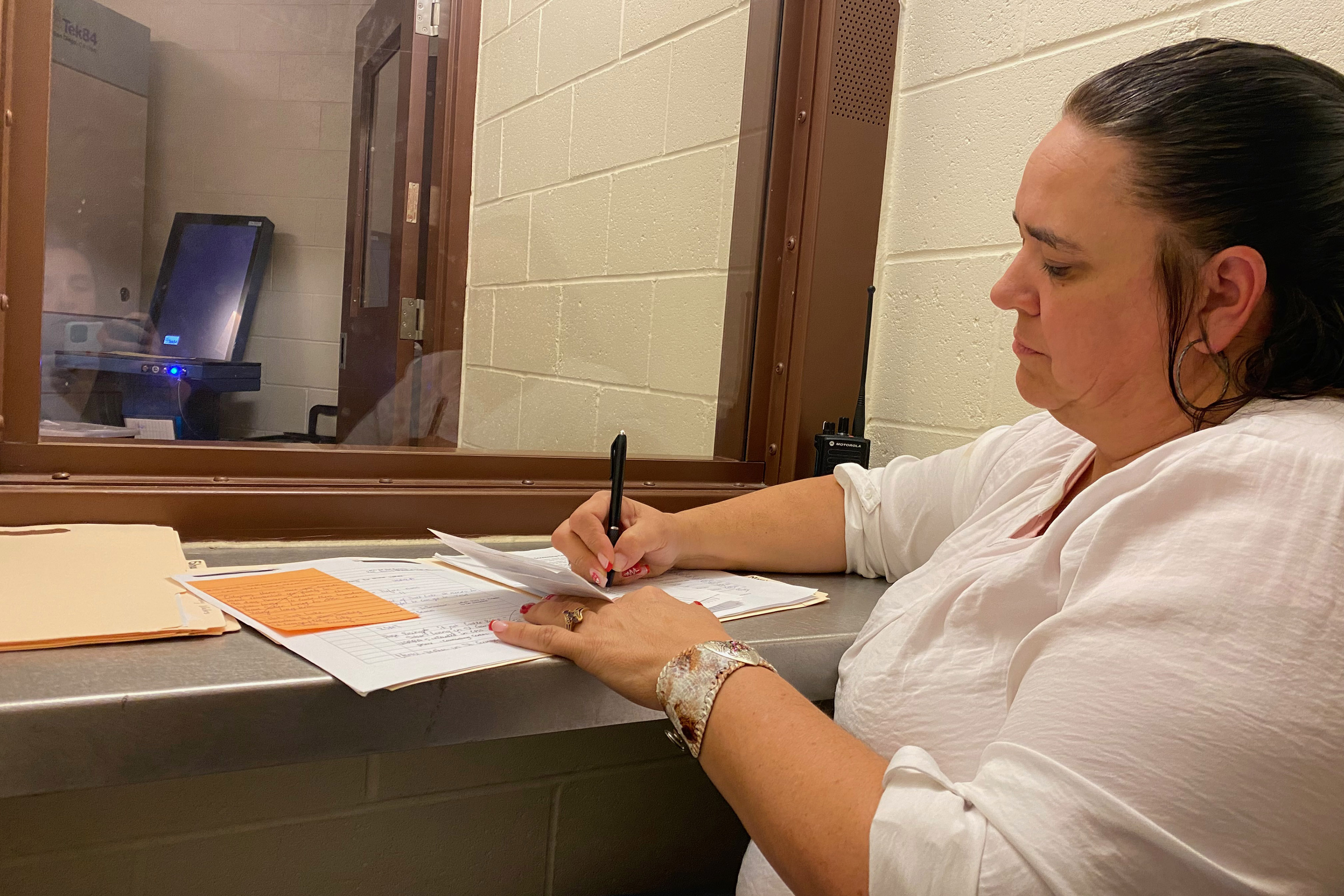 Cheryl Swapp, who is seated to the right of the frame, sits in a jail visitation room as she takes notes on standard size paper.