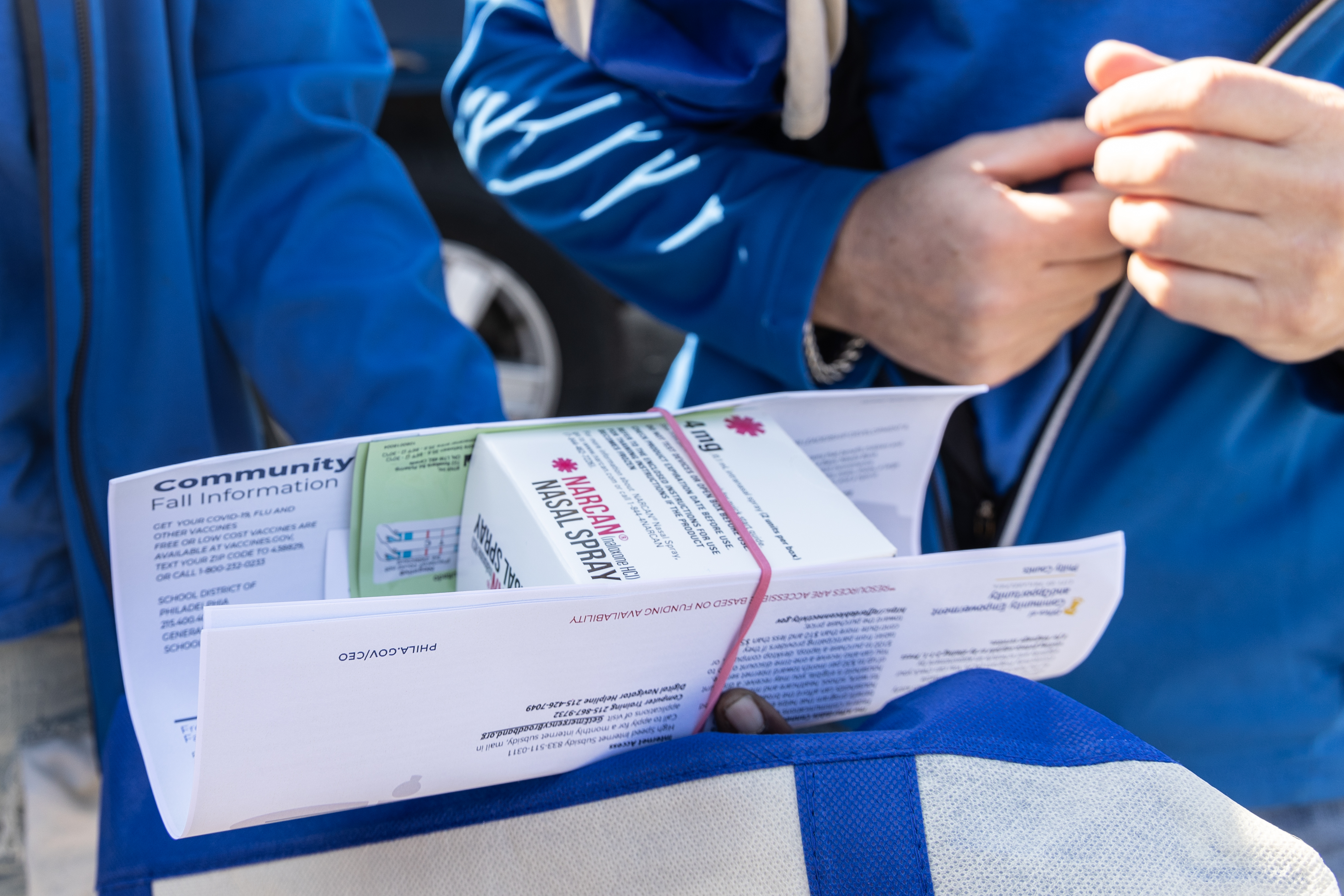 A close-up of a box of Narcan and two people in matching blue jackets holding the box