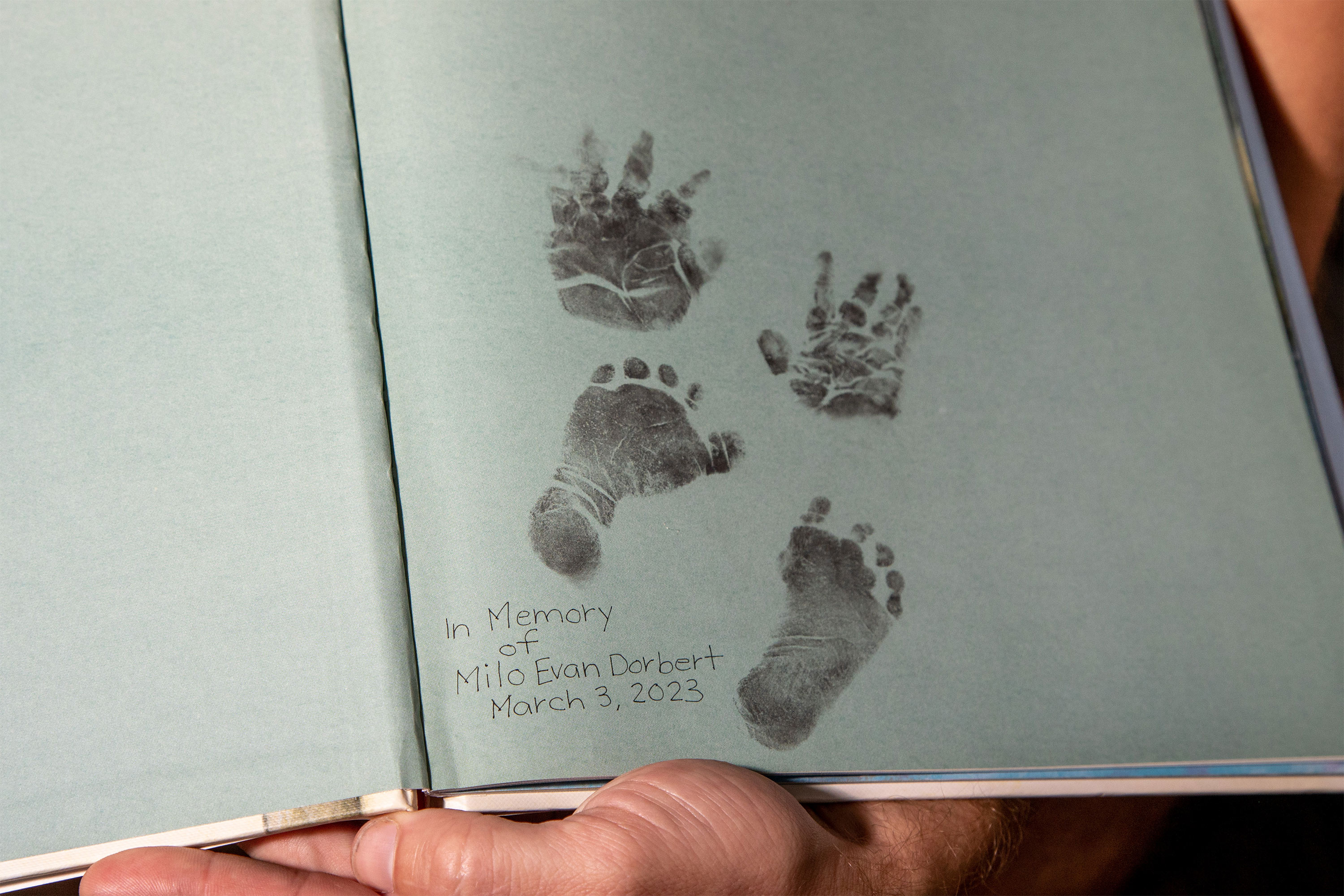 A photo of page in a boot with a baby's hand and footprints. Text near the prints reads, "In memory of Milo Evan Dorbert, March 3, 2023."