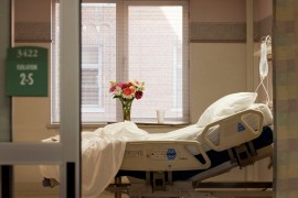 A photo showing a vacant hospital room. The bed is empty and there are flowers on the window sill.
