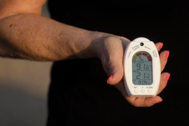 A woman holds a heat and humidity index device in her hand, facing towards the camera.