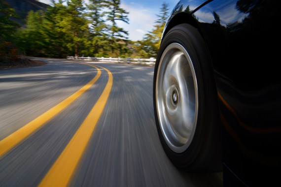 A photo of a car driving on a road, focused in on the car's tire.